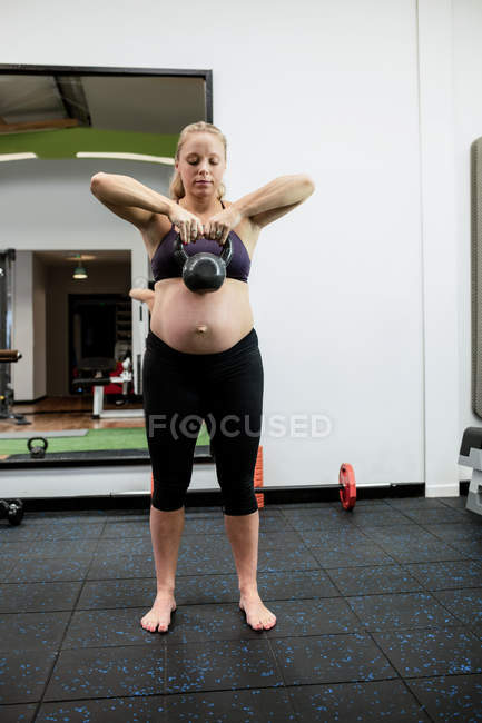 Pregnant woman lifting kettle bell in gym — Stock Photo