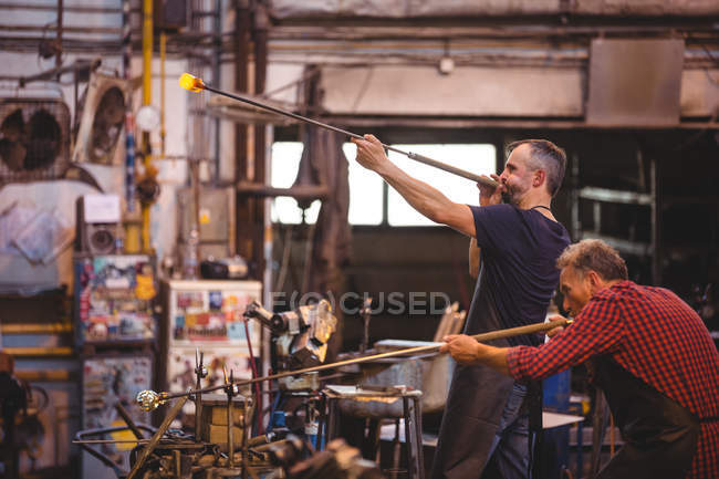 Glassblowers shaping a glass on the blowpipe at glassblowing factory — Stock Photo