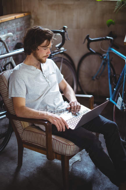 Mann sitzt auf Stuhl und benutzt Laptop in Fahrradladen — Stockfoto