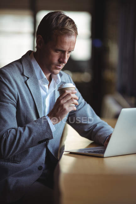 Бизнесмен пьет кофе во время работы над ноутбуком в кафе — стоковое фото
