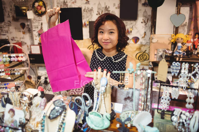 Mujer sonriente sosteniendo una bolsa rosa en una tienda de antigüedades - foto de stock