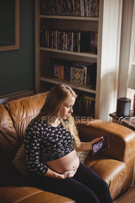 Hochwinkelaufnahme einer schwangeren Frau beim Betrachten eines Sonografiebildes auf einem Tablet im Wohnzimmer — Stockfoto