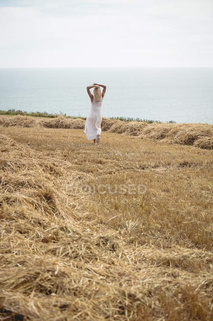 Visão traseira da mulher loira despreocupada andando no campo perto do rio — Fotografia de Stock