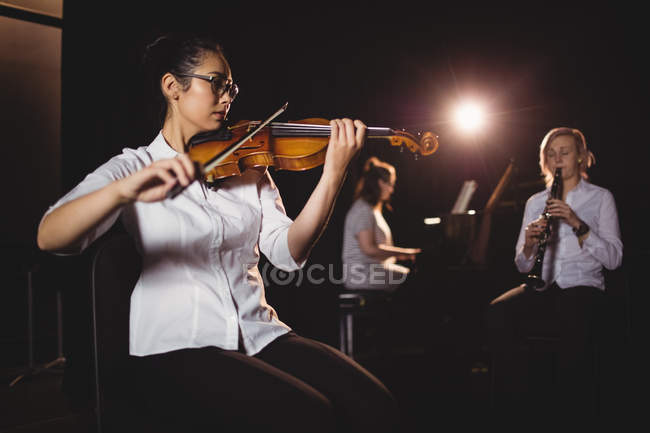 Три студентки играют на пианино, кларнете и скрипке в студии — стоковое фото