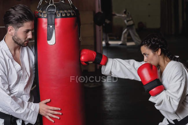 Vista lateral de deportista y deportista practicando karate con saco de boxeo en estudio - foto de stock