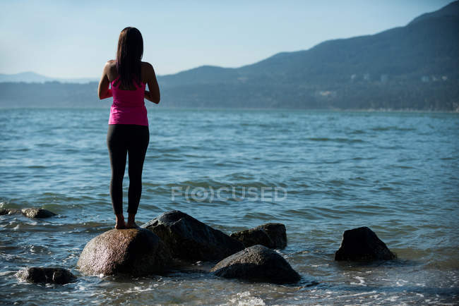 Задний вид женщины, занимающейся йогой на скале на пляже — стоковое фото