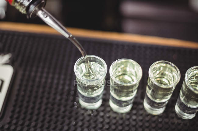 Nahaufnahme von Barkeeper, der Tequila in Schnapsgläser auf der Theke an der Bar gießt — Stockfoto
