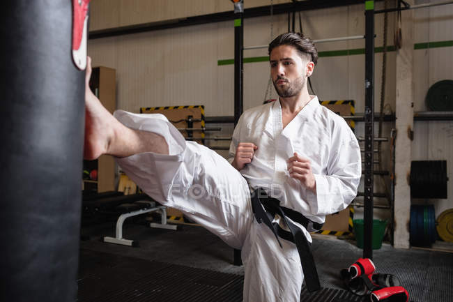 Esportivo Homem praticando karatê com saco de perfuração no estúdio de fitness — Fotografia de Stock