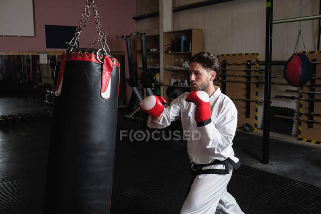 Vue latérale de l'homme pratiquant le karaté avec sac de boxe dans un studio de fitness — Photo de stock