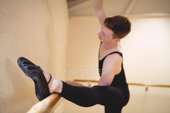 Foco seletivo de bailarino alongamento no barre enquanto pratica dança de balé em estúdio — Fotografia de Stock