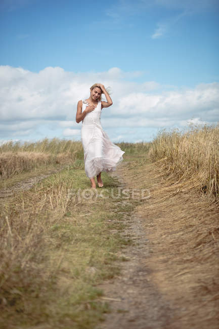 Attractive blonde woman walking on path in field — Stock Photo