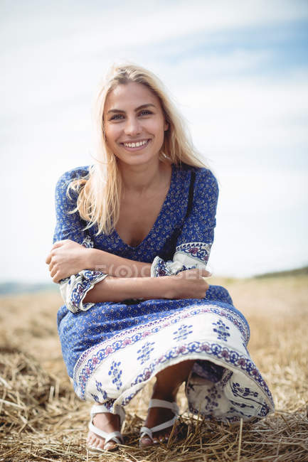Portrait of smiling blonde woman crouching in field — Stock Photo