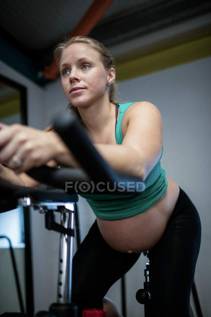 Mujer embarazada haciendo ejercicio en bicicleta estática en el gimnasio - foto de stock