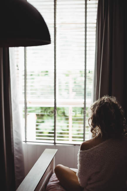 Вид ззаду жінка сидить на ліжку і дивиться крізь вікно вранці — стокове фото