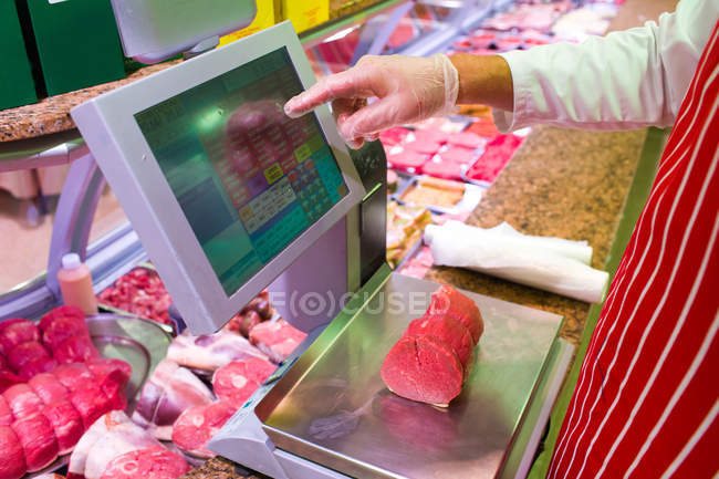 Середина м'ясника перевіряє вагу м'яса за лічильником у м'ясному магазині — стокове фото