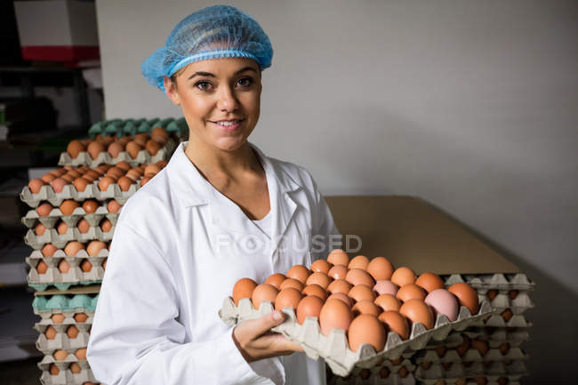 Portrait of female staff holding egg tray in factory — Stock Photo