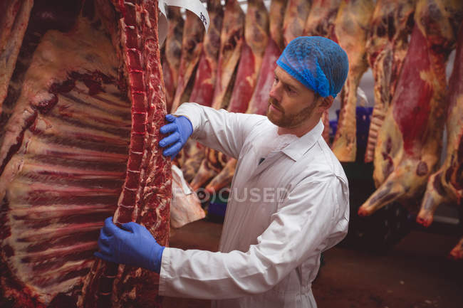 Macellaio appeso carne rossa nel ripostiglio in macelleria — Foto stock