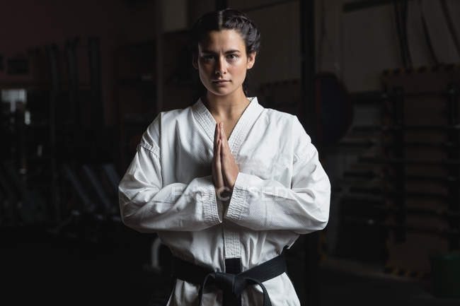 Portrait of woman in karate kimono standing with hands in namaste gesture in fitness studio — Stock Photo