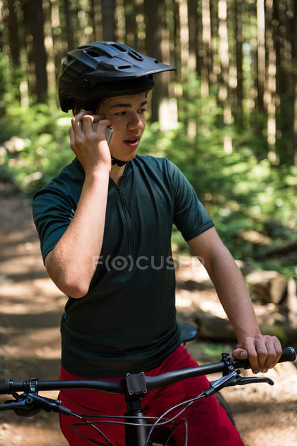 Чоловічий велосипедист розмовляє на мобільному телефоні в лісі на сонячному світлі — стокове фото