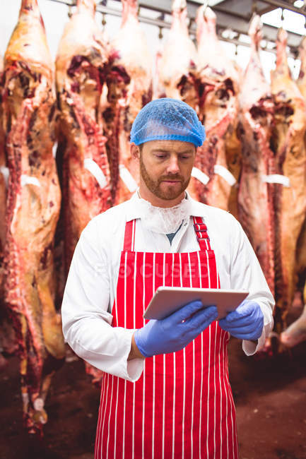 Butcher using digital tablet in meat storage room at butchers shop — Stock Photo