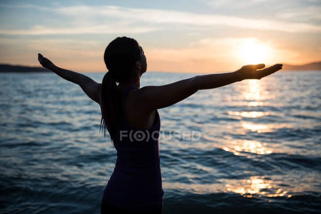 Woman performing yoga on beach during sunset — Stock Photo