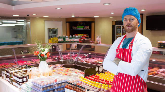 Homem açougueiro de pé em loja de carne com os braços cruzados — Fotografia de Stock