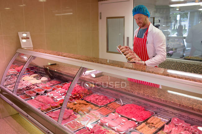 Carnicero parado en el mostrador de carne en la carnicería - foto de stock
