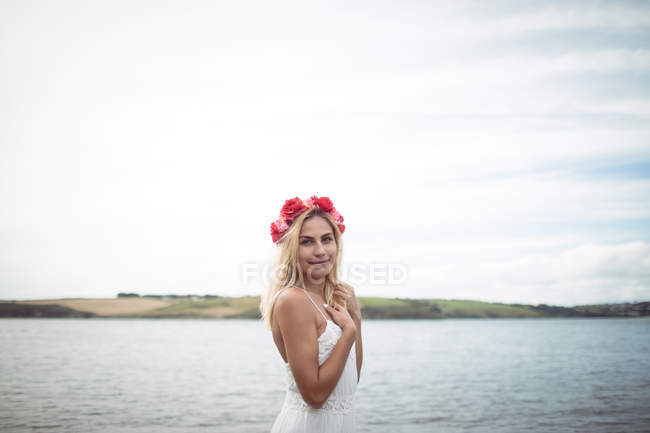 Mulher loira despreocupada em tiara flor de pé perto do rio e olhando para a câmera — Fotografia de Stock