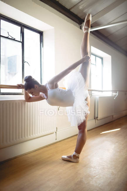 Vue latérale de Ballerina pratiquant la danse de ballet au bar en studio — Photo de stock