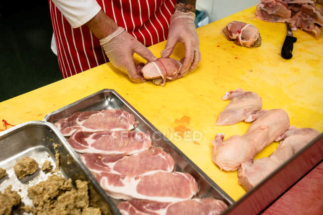 Sección media del carnicero preparando rollo de pollo y bistec en la carnicería - foto de stock