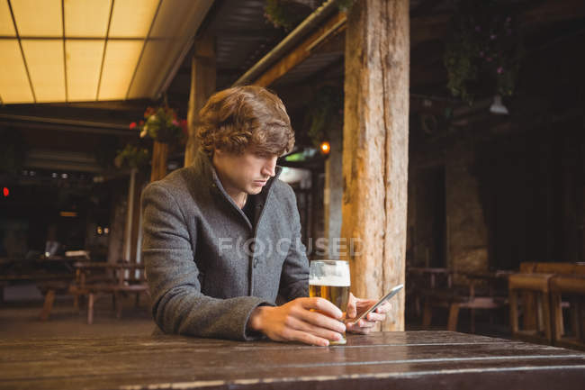 Homme utilisant un téléphone portable tout en prenant un verre de bière dans le bar — Photo de stock