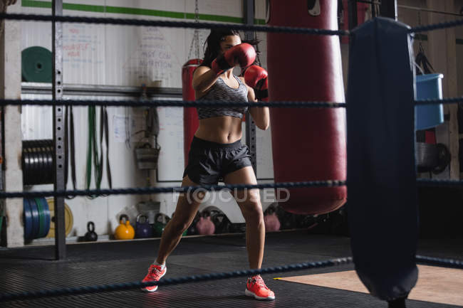 Boxer femminile che pratica pugilato con sacco da boxe in palestra — Foto stock
