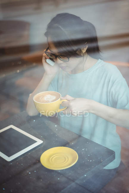Young woman talking on mobile phone while having coffee in cafe — Stock Photo