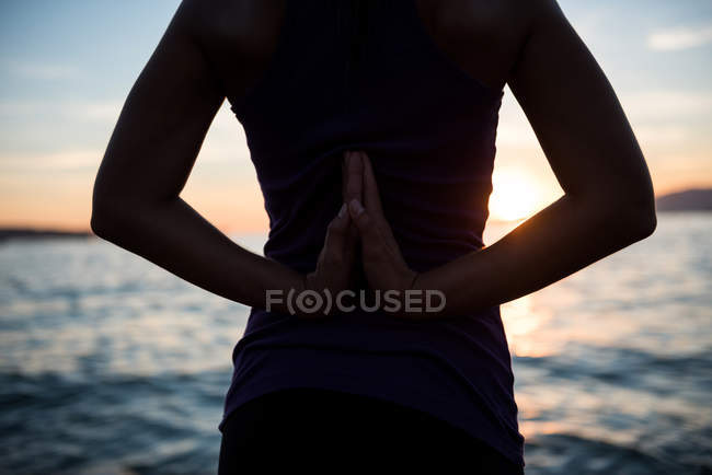 Mittelteil einer Frau, die während des Sonnenuntergangs am Strand Yoga macht — Stockfoto