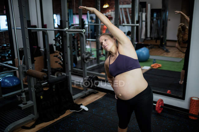 Pregnant woman performing stretching exercise in gym — Stock Photo