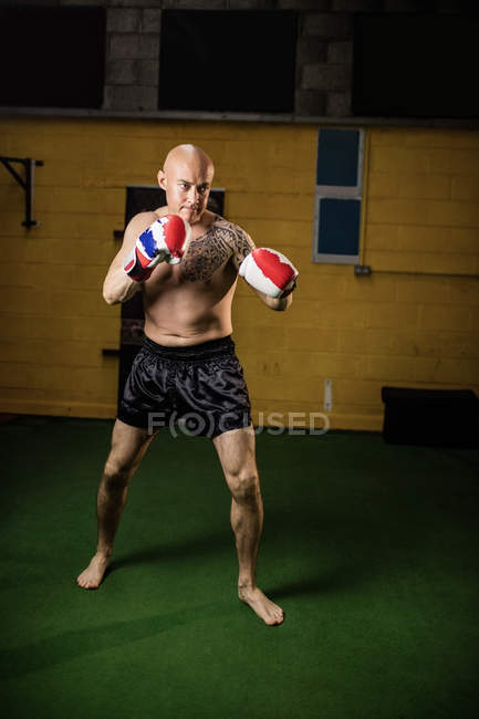 Boxeur thaïlandais tatoué torse nu pratiquant la boxe dans la salle de gym — Photo de stock