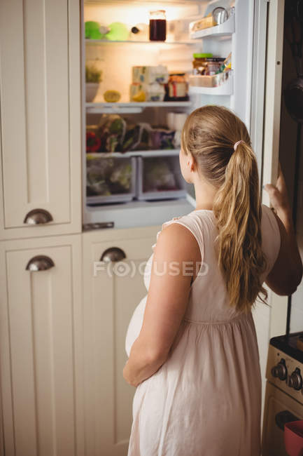 Вагітна жінка шукає їжу в холодильнику на кухні — стокове фото