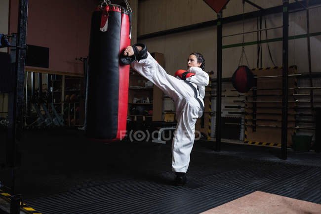 Atlético mulher praticando karatê com saco de perfuração no estúdio de fitness — Fotografia de Stock