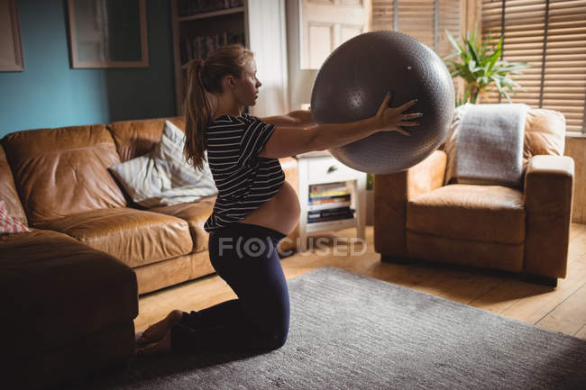 Vue latérale de la femme enceinte faisant de l'exercice avec balle de fitness dans le salon à la maison — Photo de stock