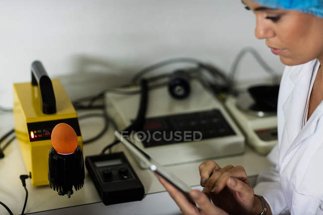 Female staff using digital tablet while examining egg on digital egg monitor in egg factory — Stock Photo