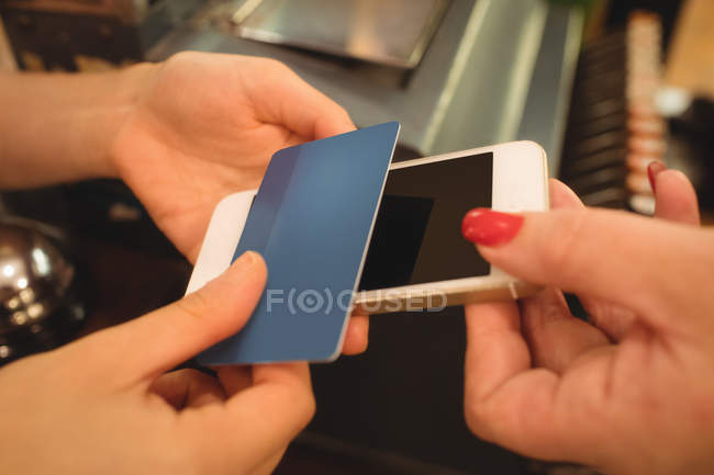 Cliente dando teléfono y tarjeta de crédito al cajero en el mostrador de facturación - foto de stock