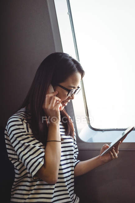 Молода жінка розмовляє на мобільному телефоні, використовуючи цифровий планшет — стокове фото