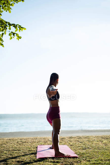 Вид сбоку на женщину, занимающуюся йогой на пляже в солнечный день — стоковое фото
