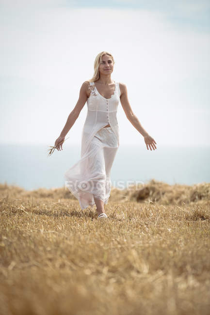 Selective focus of beautiful blonde woman walking in field near river — Stock Photo