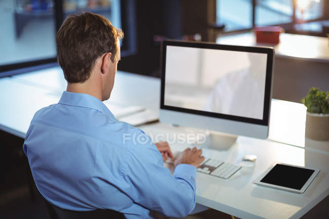 Vista trasera del hombre de negocios con PC de escritorio en la oficina - foto de stock