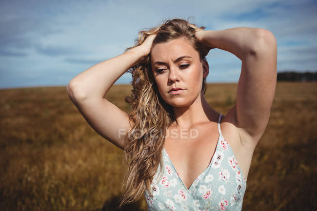 Attraente donna con le mani in capelli in piedi nel campo di grano — Foto stock