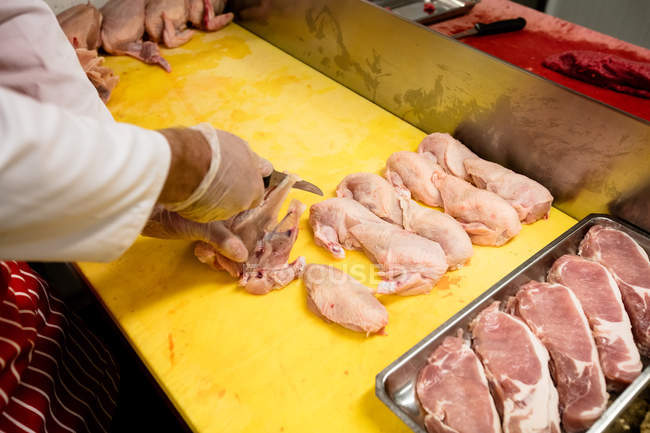 Parte média do açougueiro cortando frango no balcão de trabalho no açougue — Fotografia de Stock