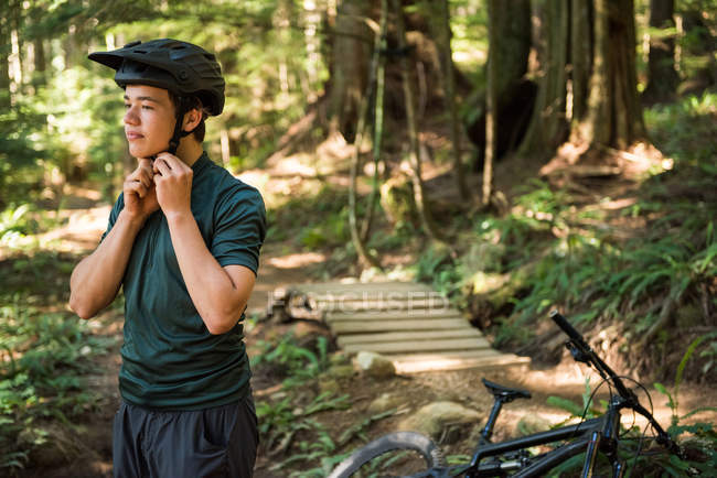 Atletico adolescente che indossa il casco da bicicletta nella foresta — Foto stock