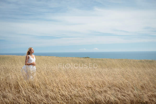 Беззаботная блондинка в белом платье стоит в поле — стоковое фото