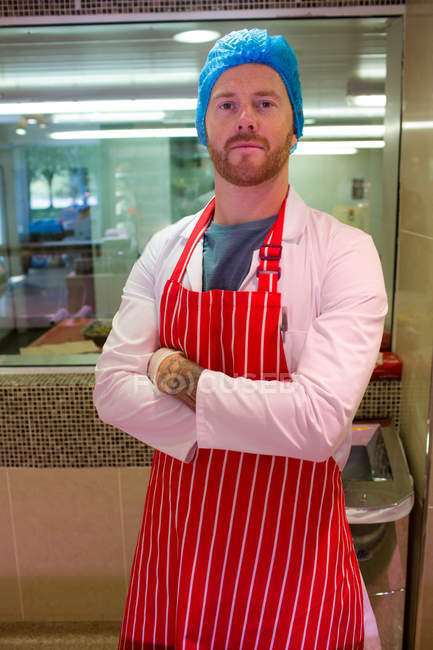 Male butcher standing in meat shop with arms crossed — Stock Photo